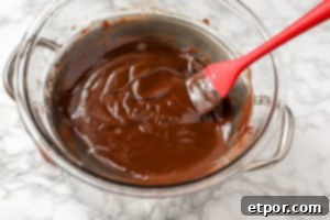 5 Malzemeli Baştan Çıkarıcı Vegan Trüf 8 A close-up view of a glass bowl filled with rich, dark vegan ganache that has just been removed from the heat. The surface is smooth and slightly glossy, indicating it's ready for the next step of chilling.
