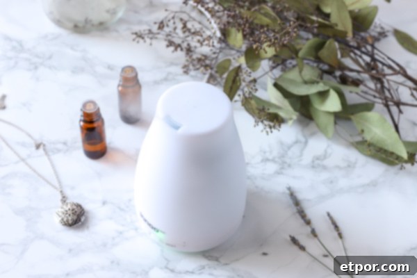 White essential oil diffuser with essential oils and eucalyptus behind it