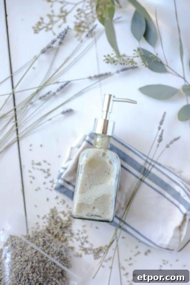Homemade face wash in a soap dispenser on a white and blue striped towel with dried lavender and eucalyptus surrounding the jar, showcasing the natural aesthetic.