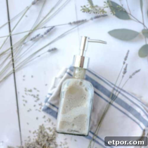 Homemade face wash in a soap dispenser on a white and blue striped towel with dried lavender and eucalyptus surrounding the jar.