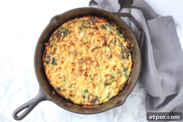 A golden brown spinach frittata in a rustic cast iron skillet, garnished with fresh herbs and placed on a grey linen napkin.