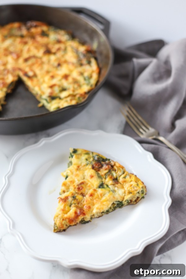A perfectly cooked slice of spinach frittata on a white plate, served with an antique fork on a grey napkin.