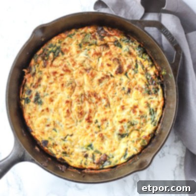 A golden brown spinach frittata in a rustic cast iron skillet, garnished with fresh herbs and placed on a grey linen napkin.