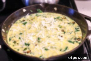 cast iron skillet with eggs, spinach, green peppers and topped with cheese for a spinach frittata