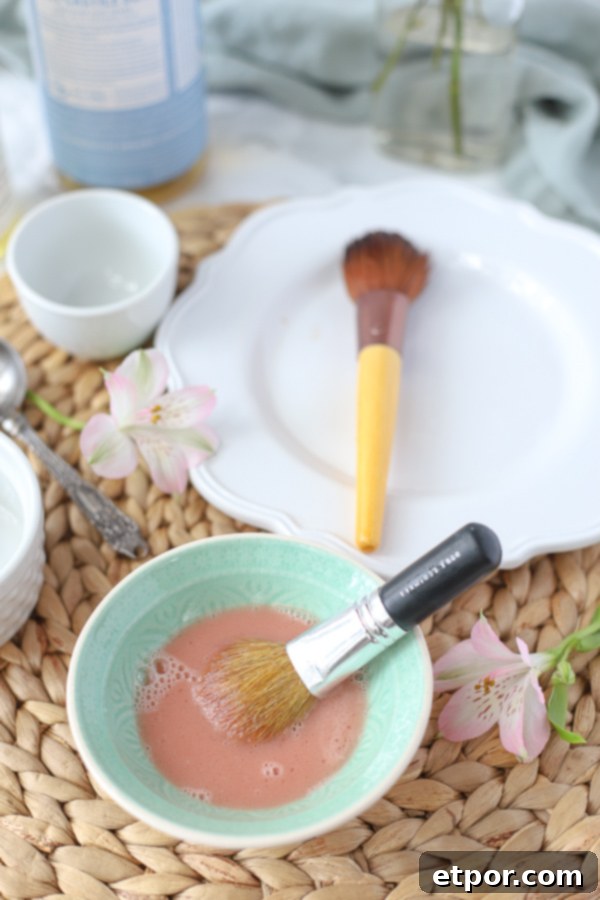 Natural Homemade Brush Wash 4 DIY makeup brush cleaner in a teal bowl with a dirty makeup brush in it and a white place with a clean makeup brush behind it