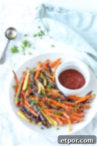 carrot fries topped with fresh herbs and cheese on white place with a small bowl of ketchup