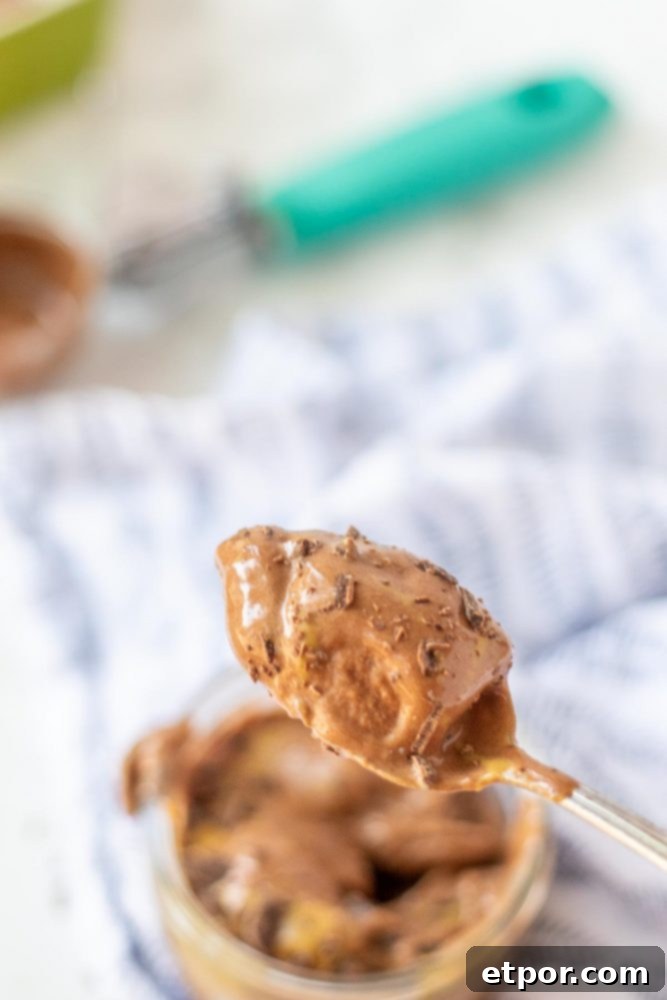 Chocolate Peanut Butter Banana Dream Freeze 3 A close-up of a spoonful of chocolate peanut butter banana nice cream, topped with a drizzle of peanut butter and chocolate shavings, in a glass dish on a patterned napkin.