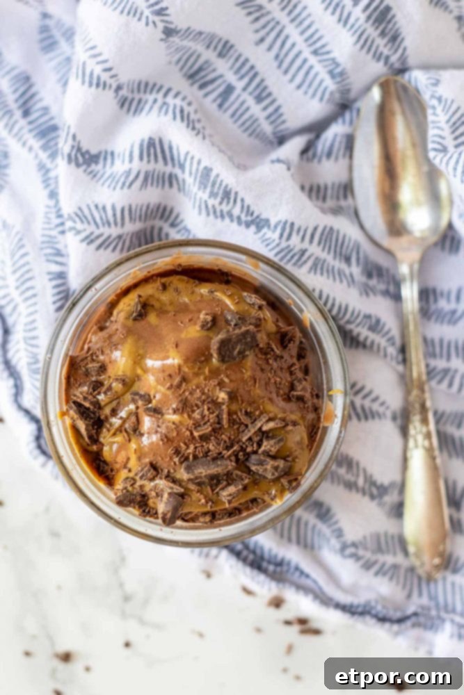 Chocolate Peanut Butter Banana Dream Freeze 4 Overhead view of a glass dish filled with chocolate peanut butter banana nice cream, garnished with peanut butter drizzle and chocolate shavings, on a blue and white patterned napkin.