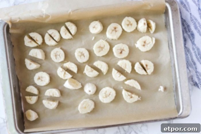 Chocolate Peanut Butter Banana Dream Freeze 6 Sliced frozen bananas arranged on a parchment-lined baking sheet, ready for blending.