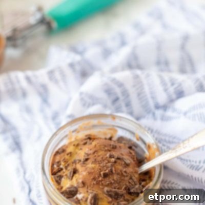 short glass dish of peanut butter and ice cream topped topped with peanut butter and chocolate shavings. An antique spoon is in the ice cream with an teal ice cream scoop in the background