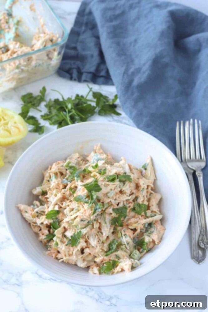 Zesty Garden Chicken Salad 3 a bowl of healthy chicken salad on a marble countertop with fresh herbs, lemon, a blue towel and forks in the background
