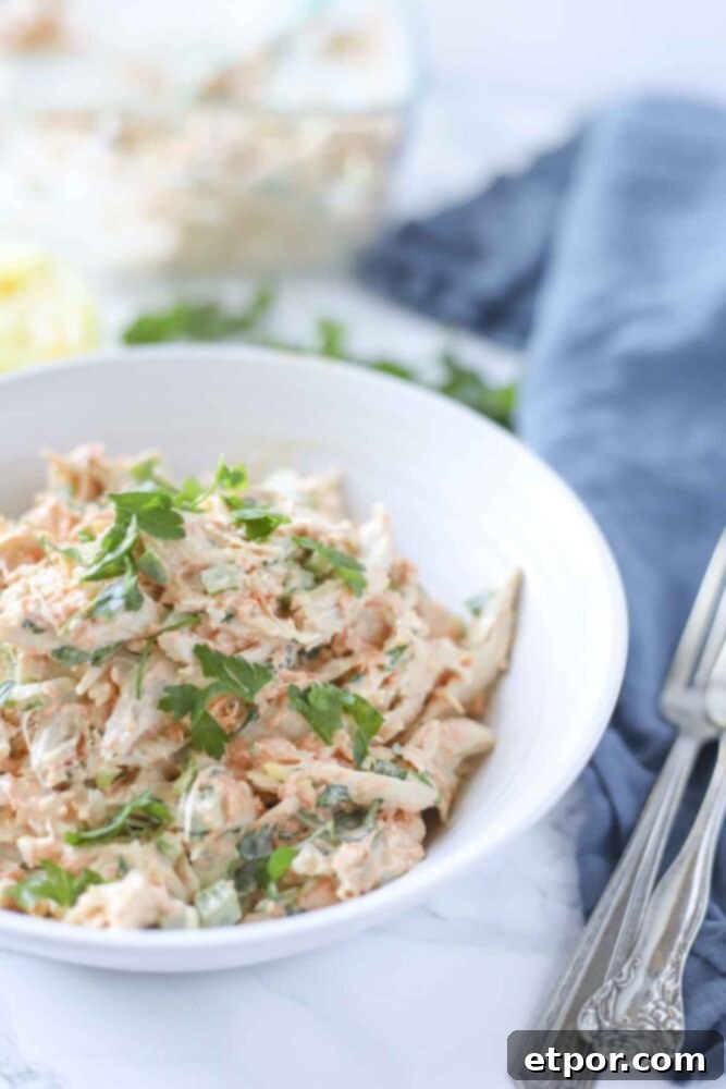 Zesty Garden Chicken Salad 5 side view of chicken salad with veggies in a white bowl with a blue towel and ingredients in the background