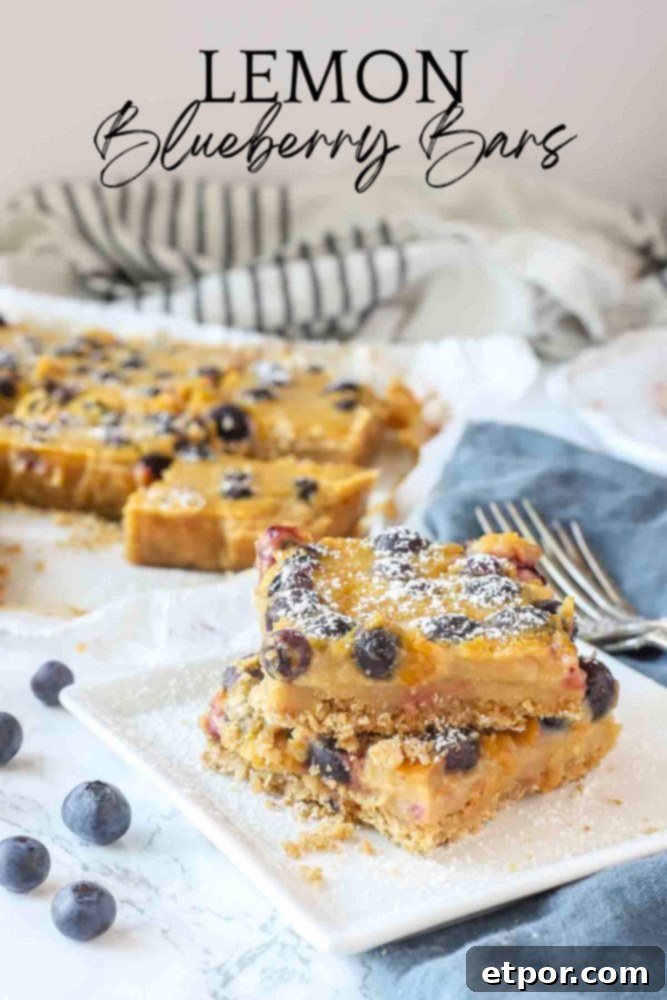 Two blueberry lemon bars stacked on a white place with a blue napkin to the right
