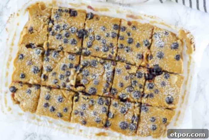 blueberry lemon bars sliced on white parchment paper with a black and white stripped towel behind it.
