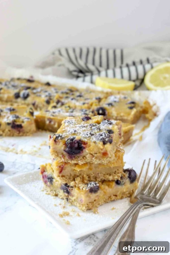 3 blueberry lemon bars stacked up on a white plate with antique forks to the right
