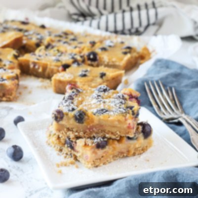 blueberry lemon bars stacked on a white plate with more dessert bars behind them