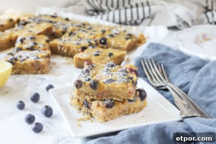 blueberry lemon bars stacked on a white plate with more dessert bars behind them
