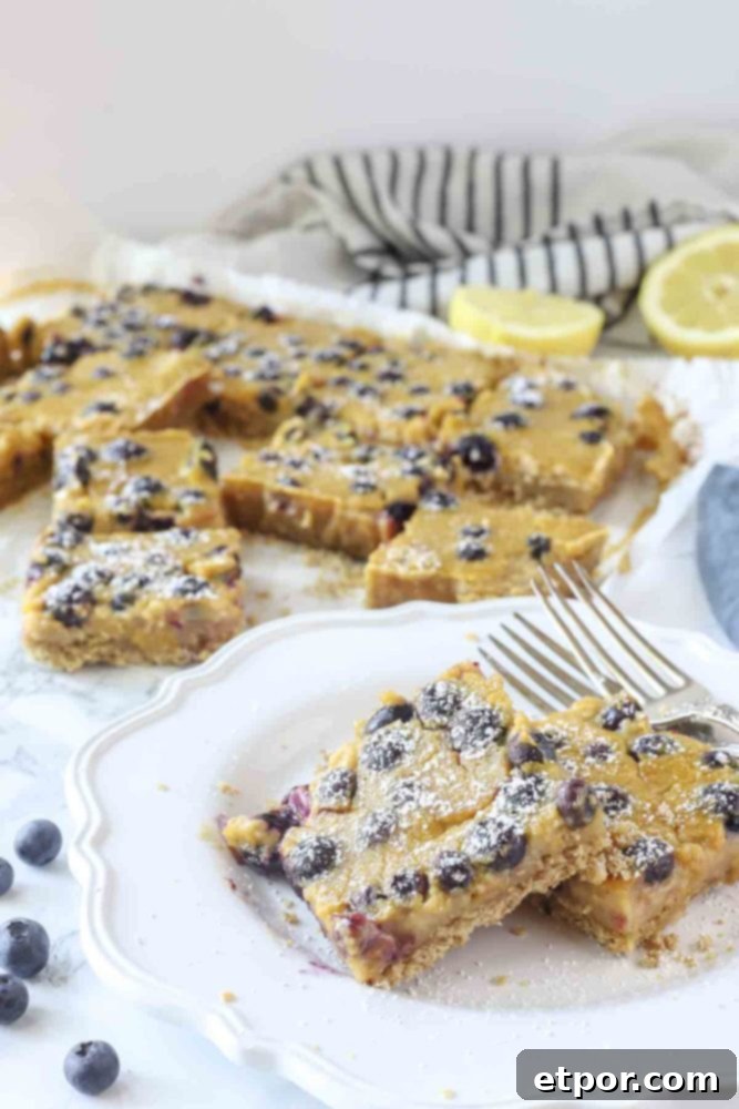 two blueberry lemon pie bars on a white plate with more bars on parchment paper in the background