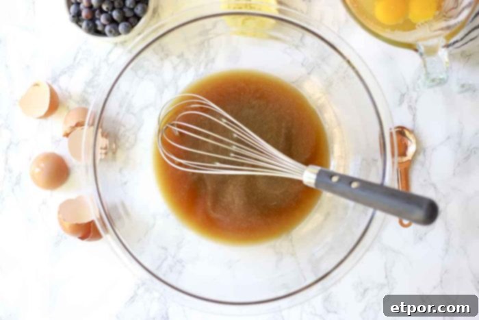 glass bowl with sugar, lemon juice and honey with a whisk in the bowl. Ingredients surround the bowl 