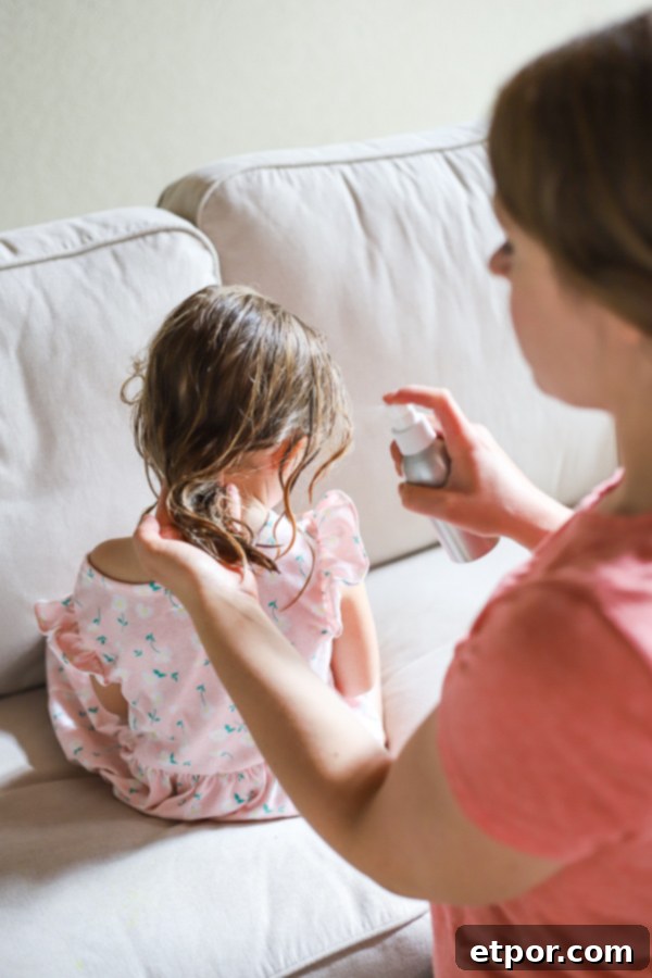 A woman gently spraying homemade natural hair detangler onto a little girl's hair, preparing to brush out tangles.