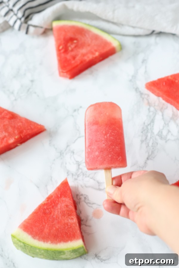 hand holding watermelon popsicles with watermelon in the backgrond