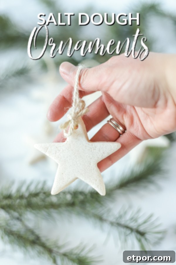 Hand holding homemade salt dough ornaments in the shape of a star with twine, with evergreens in the background.