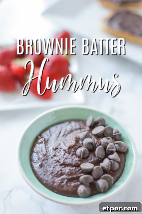bowl of brownie batter hummus topped with chocolate chips with strawberries behind it