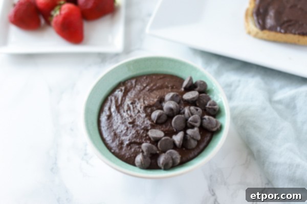 bowl of brownie batter hummus with a plate of strawberries and toast with chocolate hummus behind it