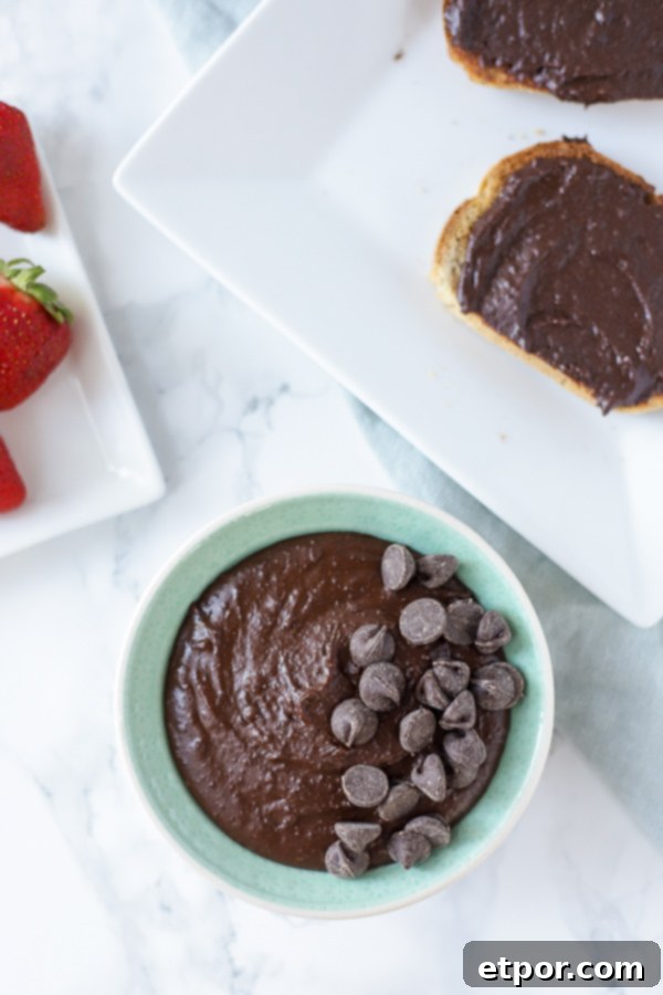 overhead shot of brownie batter hummus in a turquoise bowl and topped with chocolate chips. Two pieces of toast smothered with chocolate hummus to the back right of the bowl