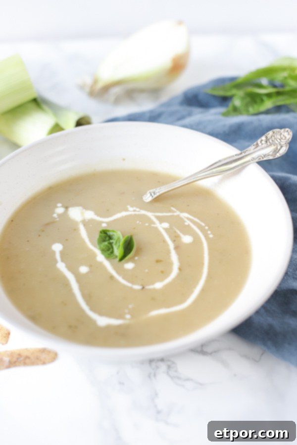Wholesome Potato Leek Soup Vegan Friendly 8 A charming close-up of a white bowl of creamy leek and potato soup, presented on a rustic blue napkin alongside an antique spoon, evoking a sense of cozy, homemade comfort.