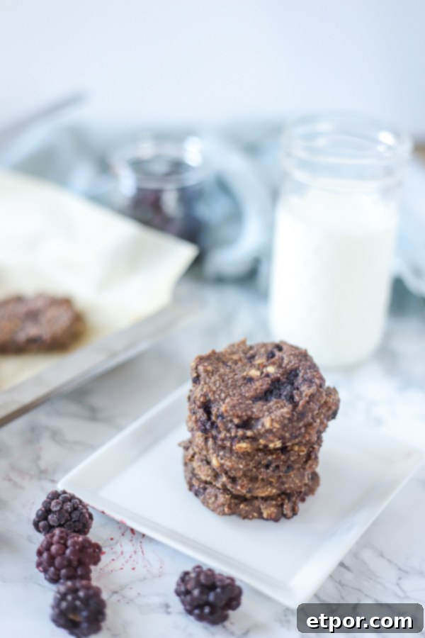 Power-Packed Blackberry Protein Cookies 11 Blackberry oatmeal protein cookies stacked on a white plate with milk behind it