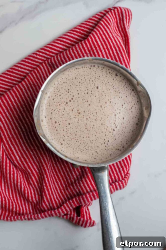 Hot chocolate mixed together in a saucepan on a red stripped towel.