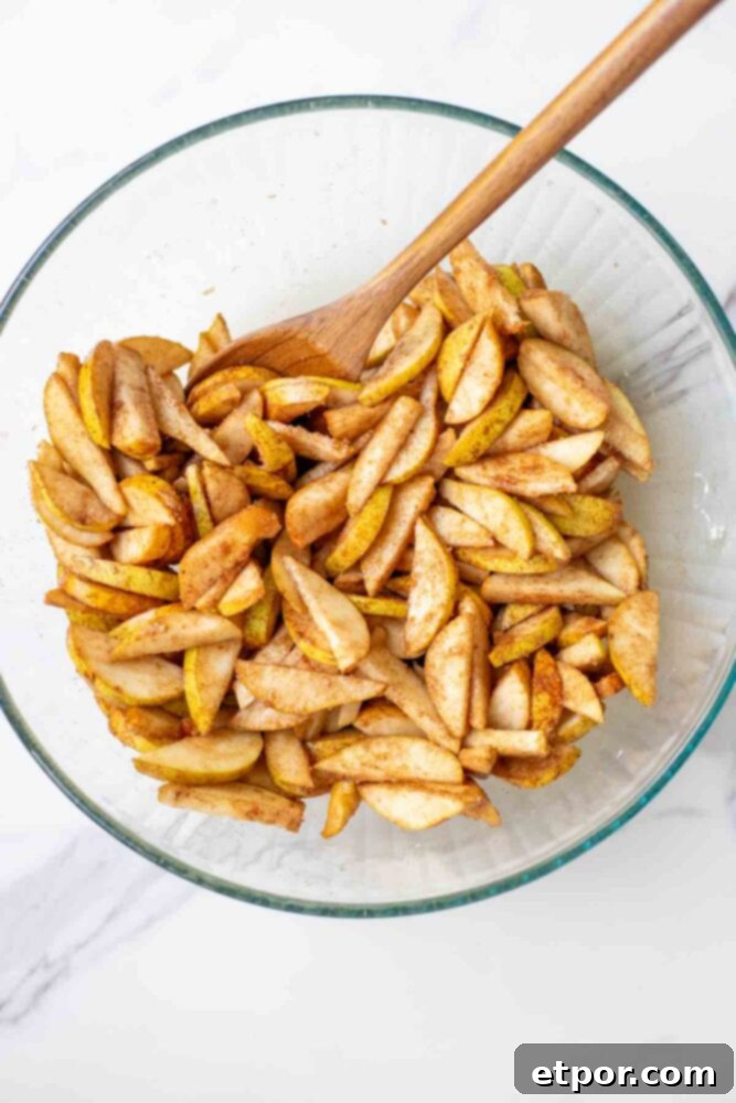 Sliced pears mixed with spices, brown sugar and cornstarch in a glass bowl with a wooden spoon.