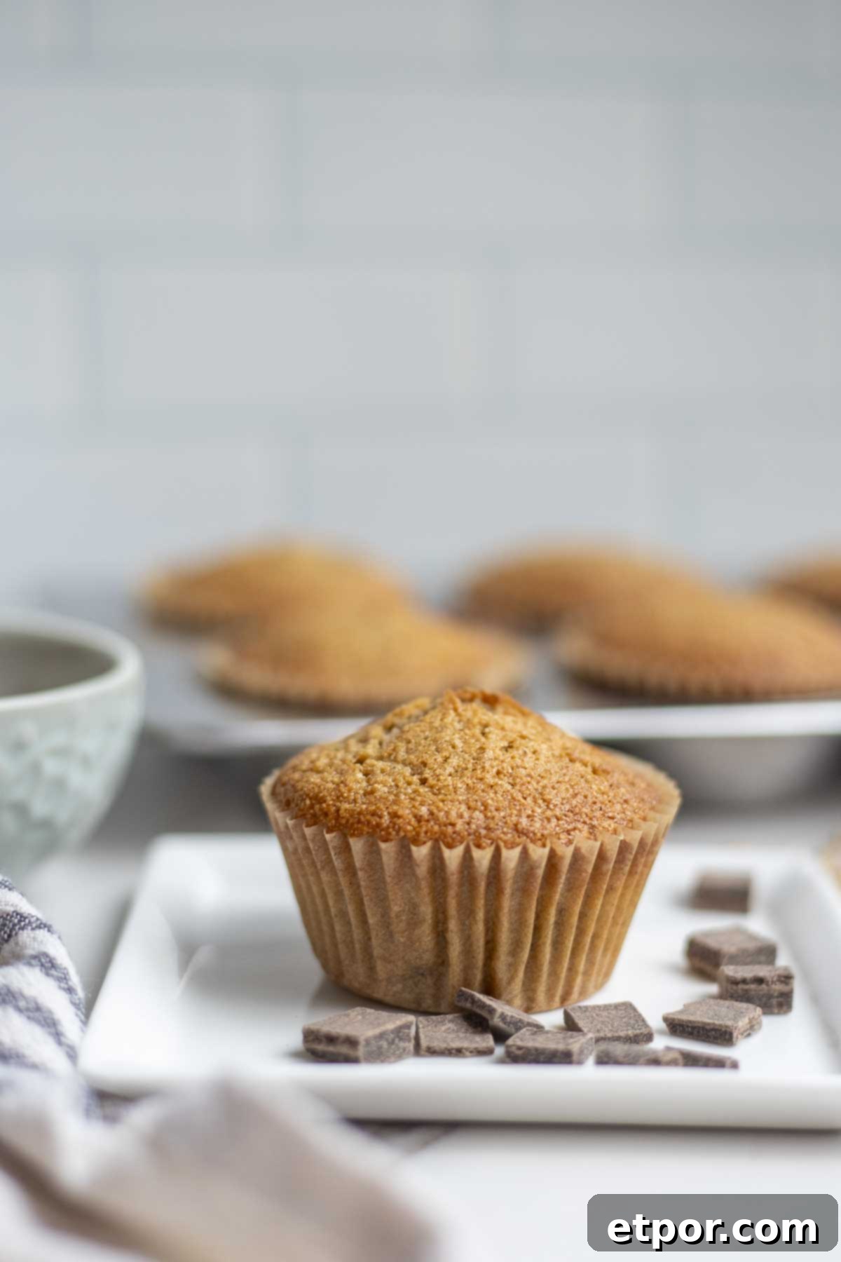Artisan Chocolate Chunk Muffins with Whole Grain Sourdough 9 Whole wheat sourdough chocolate chip muffin on a plate surrounded by chocolate chips with more muffins in the background.